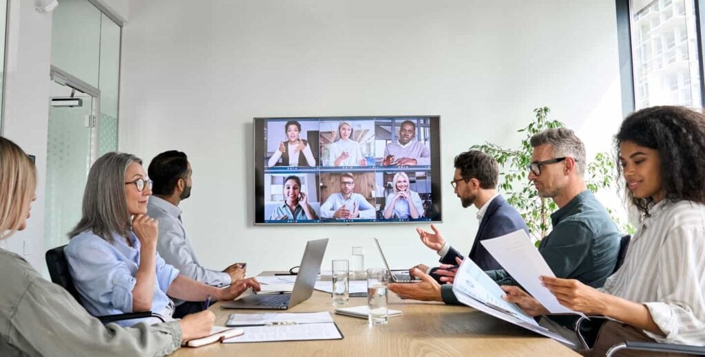 6 people sitting around a boardroom table utilising a boardroom meeting room system that is connected to the TV on the wall. 